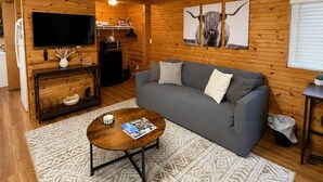 En mysig stuga med träpanel i taket, en grå soffa, ett soffbord och en tv på väggen.