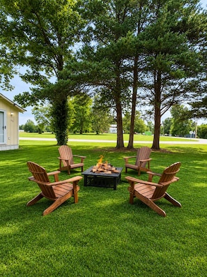A patio area with four Adirondack chairs arranged around a square fire pit.