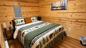 En stuga med träpanel, inredd med en säng, ett nattduksbord, en lampa, en väggmonterad värmare och en tavla som föreställer en skogsmiljö.