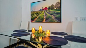 A dining area with a glass table, four dark placemats, and a central candle holder with candles. A framed landscape painting is on the wall above. - Fun Getaway?Georgetown Speakeasy/private bar(BYOB)hot tub/pool table/Bourbon Trl (Georgetown)