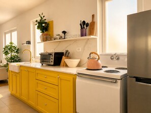 Eine Küche mit gelben Schränken, einem weißen Herd, einem pinkfarbenen Wasserkocher und einem Toaster.