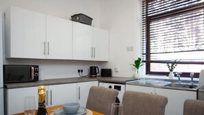 Een compacte keuken met witte kastjes, een magnetron, een koffiezetapparaat en een eethoek met een tafel gedekt voor twee personen.