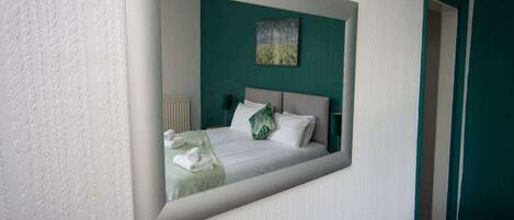 A bedroom with a bed, a green wall, and a painting.