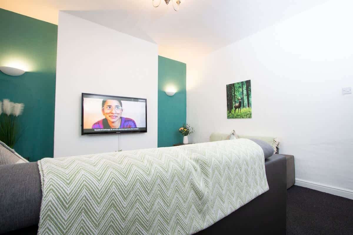 Um quarto com uma cama, uma televisão fixada na parede e uma fotografia de uma floresta.