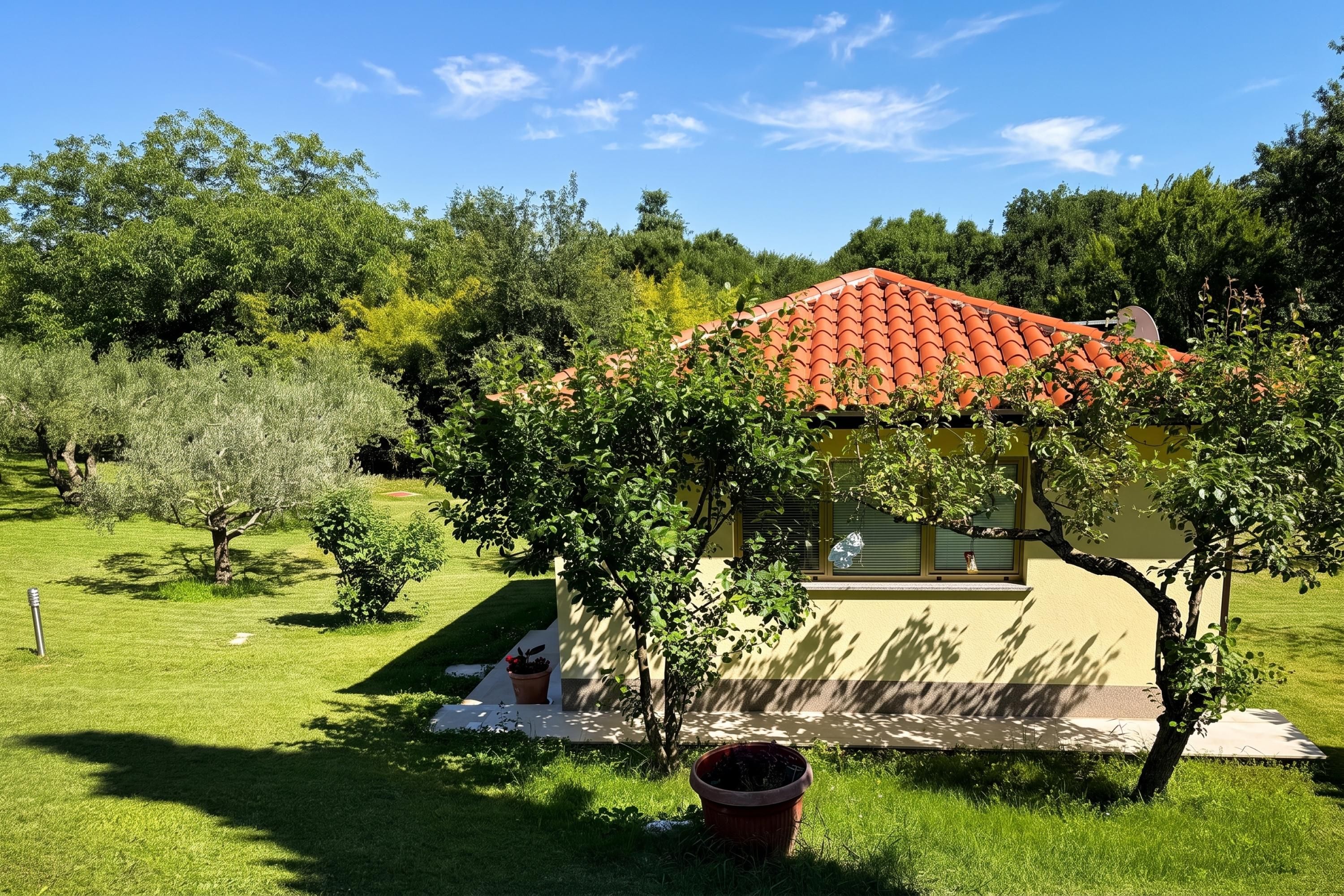 A small house with a red-tiled roof, surrounded by lush greenery and trees.