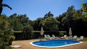 Piscina com espreguiçadeiras e guarda-sóis, rodeada por vegetação.