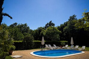 Ein Schwimmbecken mit Liegestühlen und Sonnenschirmen, umgeben von viel Grün.