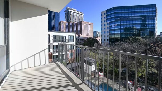 Un balcón con vista a un paisaje urbano, incluyendo edificios modernos y una piscina.