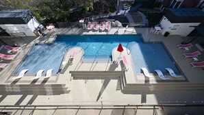 Una piscina con varias pistas, tumbonas y una sombrilla roja.