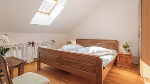 A bedroom with a wooden bed, a small bedside table, a chair, a window with a view, and a ceiling light.
