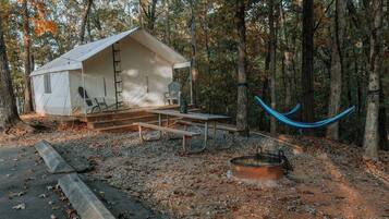 A rustic cabin with a porch, a hammock, and a fire pit.