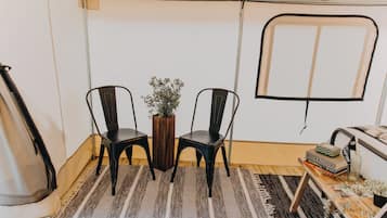 Une petite pièce avec deux chaises, une table, une plante en pot, un tapis et une fenêtre à cadre noir.