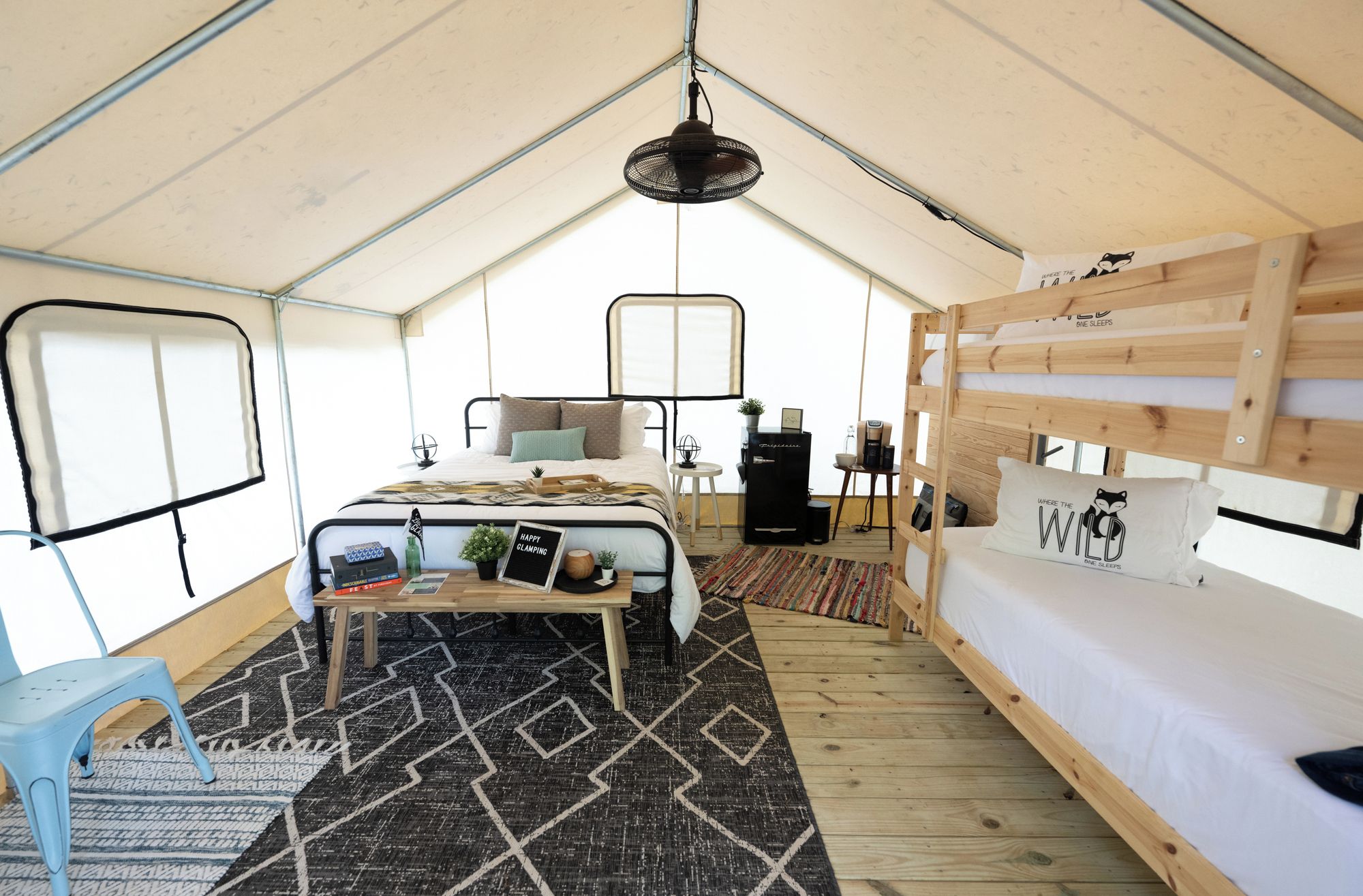 A tented accommodation with a bunk bed, a small table with a plant, and a bed with a pillow featuring a wild animal design.