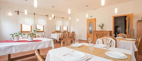 Een eethoek met tafels gedekt voor vier personen, houten stoelen, hanglampen en uitzicht op de eetruimte.