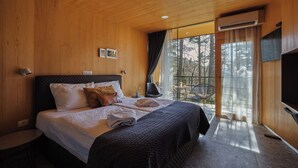Een slaapkamer met houten lambrisering, een bed, een televisie en een balkon met een stoel.