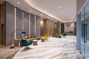 Un vestíbulo moderno con suelo de mármol, un sofá, un sillón amarillo y una recepción.