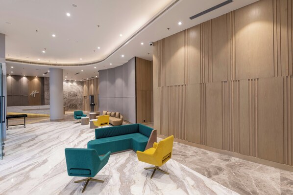 Un lobby moderno con techo curvo, suelo de mármol y una zona de estar con sillas verde azulado y amarillas.