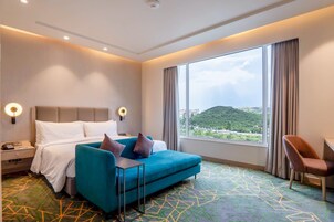 Habitación de hotel con cama, escritorio, silla y una ventana grande con vistas.