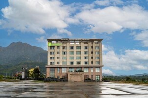Un hotel de varios pisos con fachada plana, entrada visible y estacionamiento frente a él.