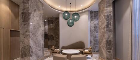 Um lobby moderno com piso de mármore, uma mesa redonda com cadeiras e uma coluna grande.