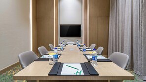 A conference room with a long table, chairs, water bottles, nameplates, and a TV screen. - Holiday Inn Katra Vaishno Devi (Reasi)