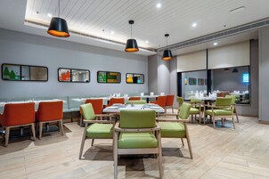 Un comedor moderno con varias mesas y sillas, iluminación colgante y cuadros en la pared.