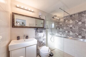 A bathroom with a white sink, a mirror, a shower with a glass door, and patterned tiles. - Punta Debij Studio Laura, Punat, Croatia (Punat)