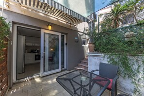 Eine Terrasse mit Tisch und Stühlen, eine Schiebetür zu einer Küche und eine Treppe, die zu einer oberen Ebene führt.