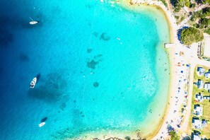 An aerial view of a beach with clear turquoise waters, a few boats, and a row of beachside cottages. - Punta Debij Apartment Natasa, Punat, Croatia (Punat)
