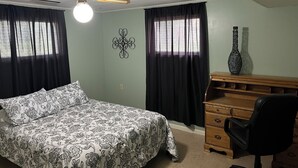 A bedroom with a bed, a desk, a chair, a dresser, a ceiling fan, and a wall decoration.