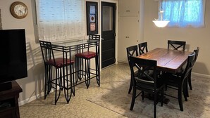 A dining area with a wooden table and chairs, a clock on the wall, and a framed family message.