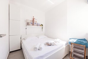 A minimalist bedroom with a bed, a shelf with decorative items, and a small wooden side table. - Punta Debij Apartment Andrea, Punat, Croatia (Punat)