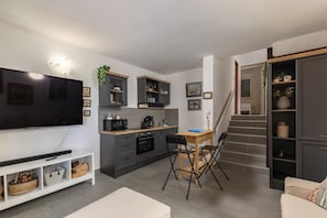 A modern kitchen with a flat-screen TV, grey cabinets, and a dining area with a table and chairs. - Punta Debij Apartment Andrea, Punat, Croatia (Punat)