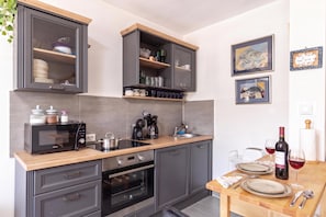 Een moderne keuken met grijze kastjes, een houten aanrecht, een inbouwoven, een koffiezetapparaat, en een eethoek met een tafel gedekt voor twee personen.