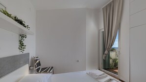 Una habitación de hotel moderna con cama, ventana con cortinas, una pequeña mesa y una silla.