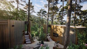 Uma cabana na floresta com um deck de madeira, uma escadaria e um espaço de estar.