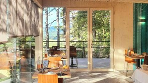 Uma sala de jantar moderna com paredes de vidro, móveis de madeira e vista para o exterior.