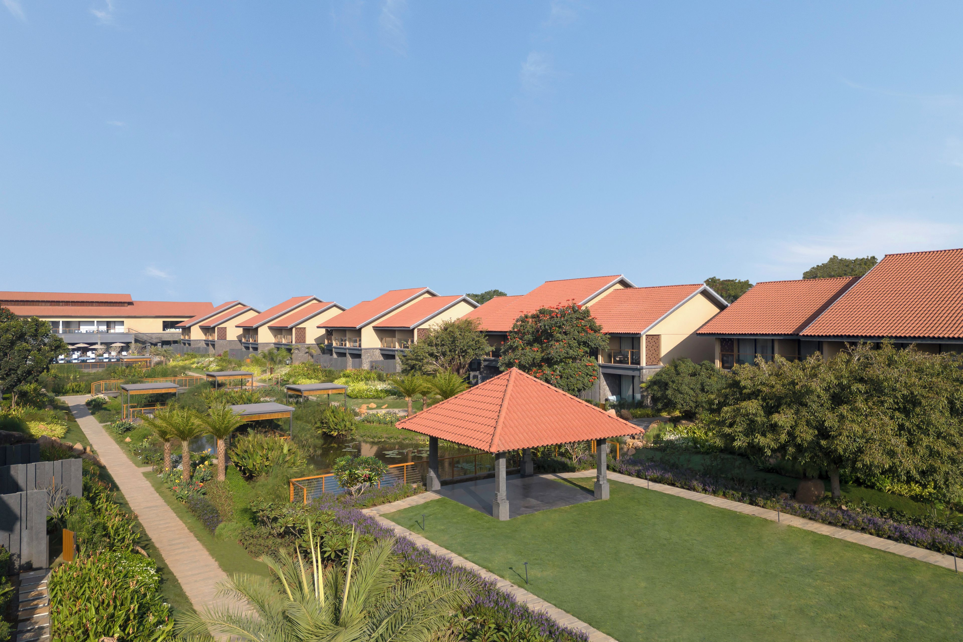 Filare di edifici di un hotel con tetti rossi, un'area giardino centrale e un vialetto che conduce a un gazebo.