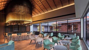 A modern bar area with a curved ceiling, seating with round tables, and large windows offering views of the cityscape.