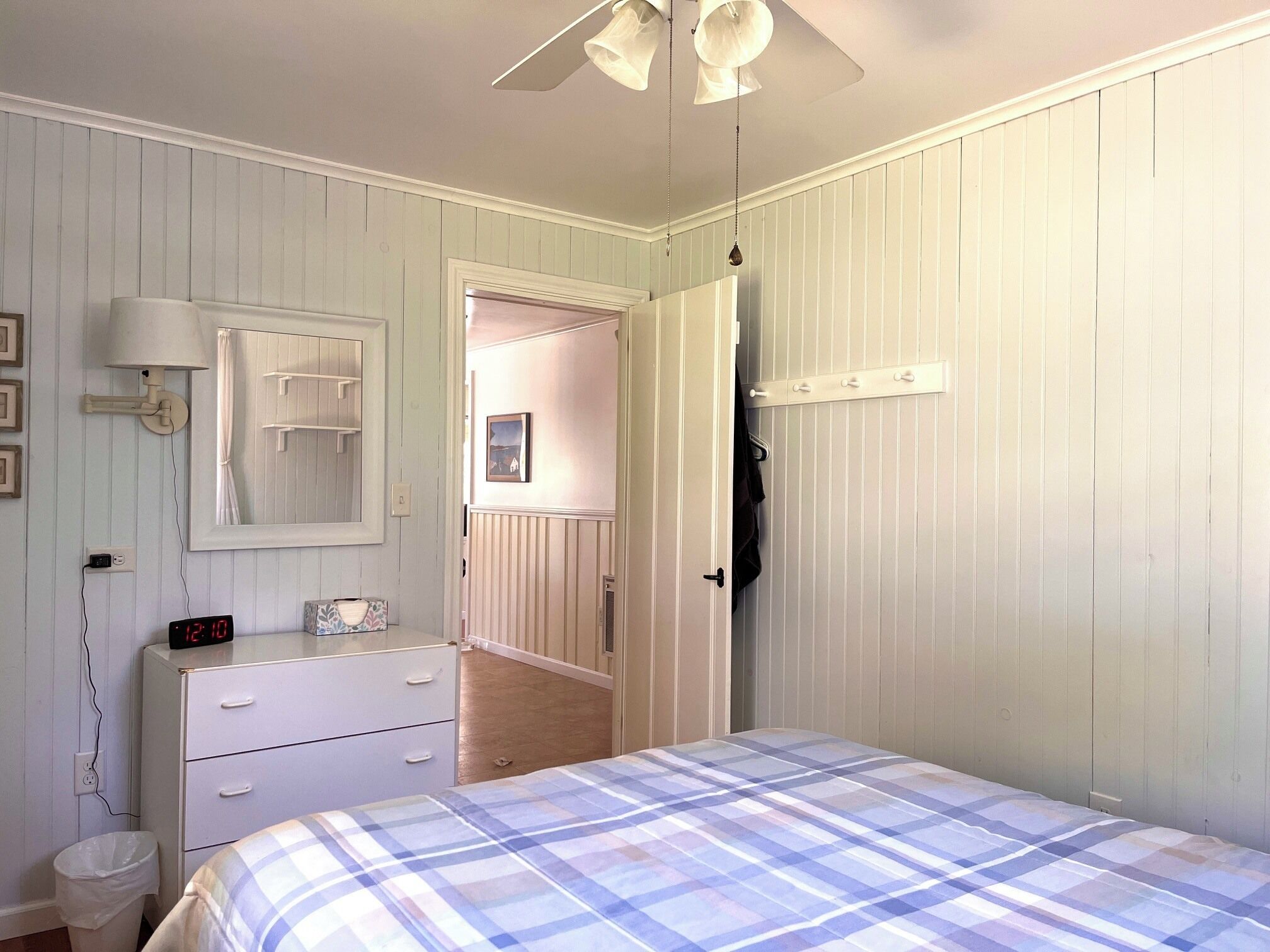Un dormitorio con cama, cómoda, mesita de noche, espejo y ventilador de techo.