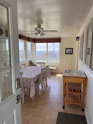 Un comedor con una mesa y sillas, un ventilador de techo, una ventana con vistas y una pequeña mesa de madera.