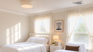 A bedroom with two beds, a nightstand with a lamp, a framed picture, and a window with curtains. - beach front bliss: 2Br apartment in peaceful Quincy near Backbay (Quincy)
