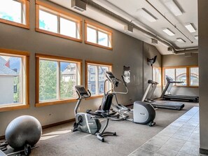 A gym with exercise equipment, large windows, and a view of buildings outside. - Charming Alpine Penthouse [Heated Pool & Hot Tubs] (Canmore)