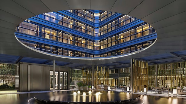 Ein modernes Gebäude mit einem kreisförmigen Atrium, einer Wasserspiele-Anlage in der Mitte und Sitzbereichen am Rand.