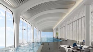 Ein moderner, überdachter Poolraum mit gewölbter Decke, großen Fenstern und Liegestühlen.