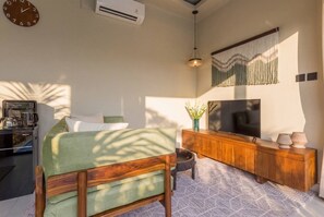A modern living room with a sofa, a coffee machine, a TV, and a decorative wall hanging. - Vinyak Villa (Kerobokan)