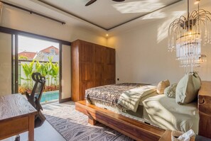 A bedroom with a bed, wooden furniture, a desk, and a view of a swimming pool. - Vinyak Villa (Kerobokan)