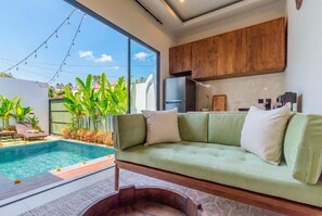A modern living area with a pool, a green sofa, wooden cabinets, and a view of the outdoors. - Vinyak Villa (Kerobokan)