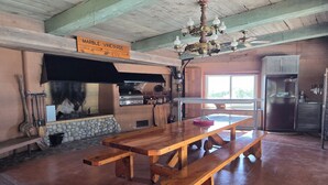 A rustic kitchen with a stone fireplace, wooden benches, a chandelier, and a refrigerator.