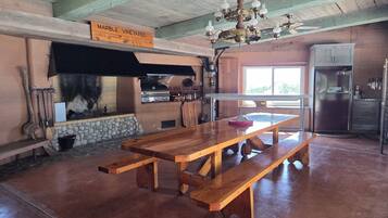 Une cuisine rustique avec une cheminée en pierre, des bancs en bois, un lustre et un réfrigérateur.